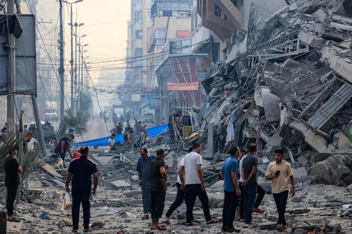 Men walk among collapsed buildings and debris strewn across the street